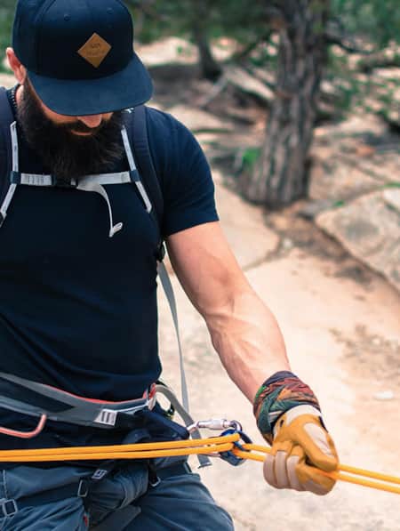 A man outside, wearing a climbing harness, is belaying himself.