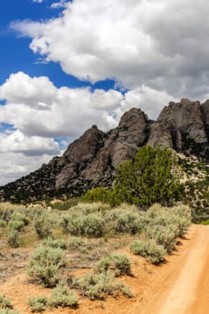 An orange-hued dirt road with sparse vegetation on each side, leading towards a grey, rocky mountain.
