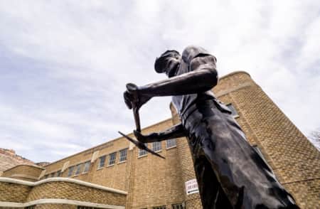 A metal statue of a railroad worker located in front of a library.