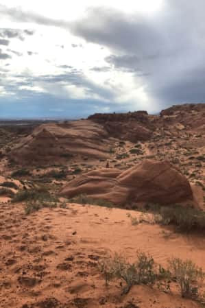 A scenic landscape of sand, sparse vegetation, and various red rock formations.