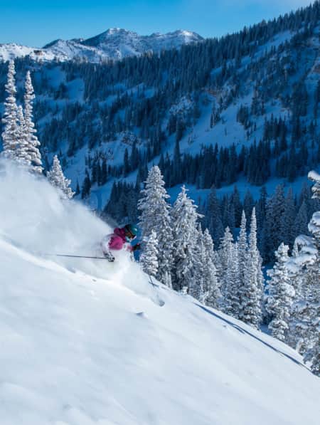 A skier making a turn down a snowy mountain, kicking up a spray of snow behind them.
