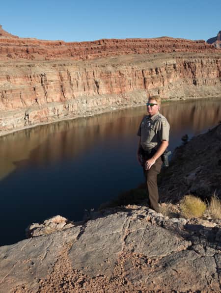 A park ranger standing on top of a large rock formation, looking out over a wide river.