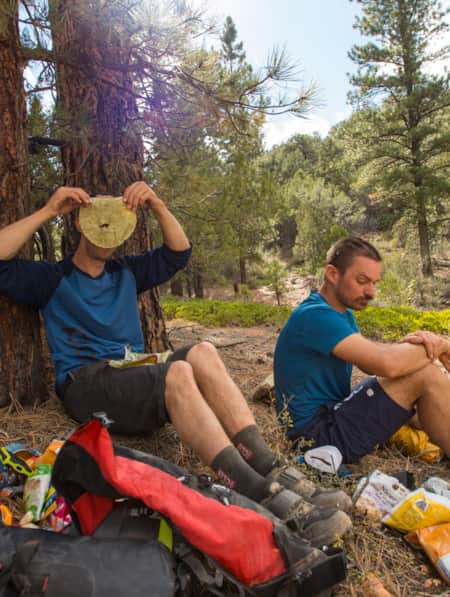 Two mountain bikers resting under a tree, eating a snack.