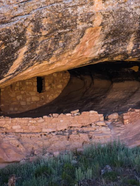 Ruins built inside a large cave within a slab of red rock.