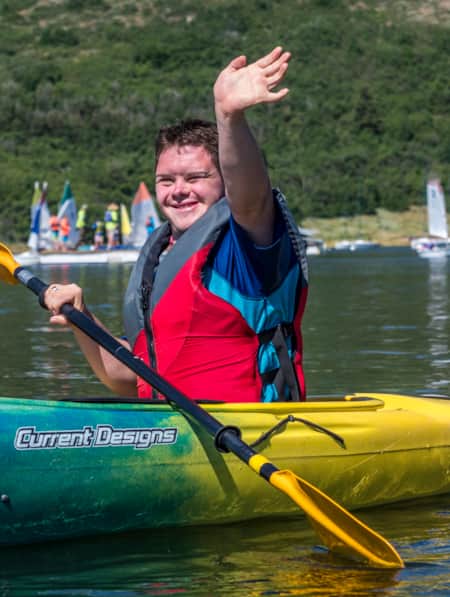 A person inside a kayak on a lake, smiling and waving.