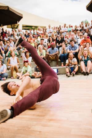 A man break dancing on a stage, surrounded by a cheering crowd.