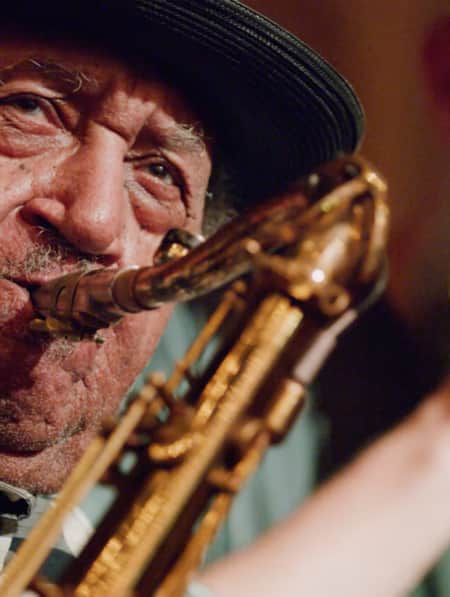 A man playing the saxophone with another man behind him singing into a microphone.