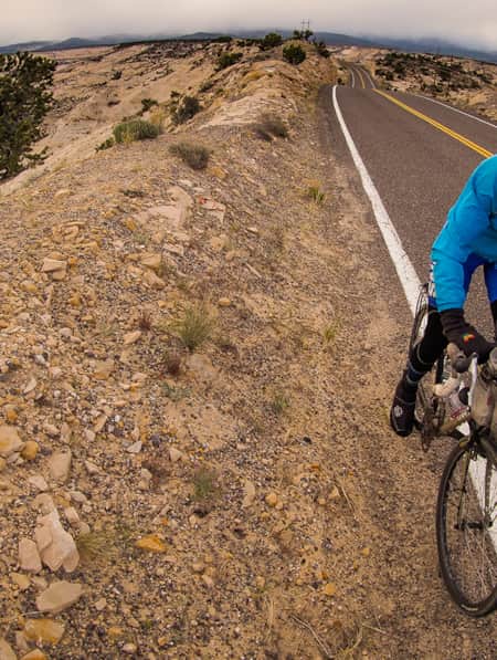A person cycling along the side of a road through a landscape of large, rocky hills.