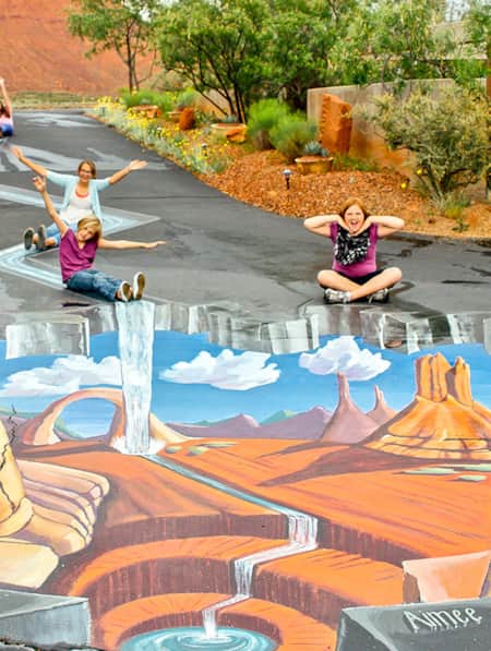 Women and children posing around a three-dimensional chalk painting on the ground.