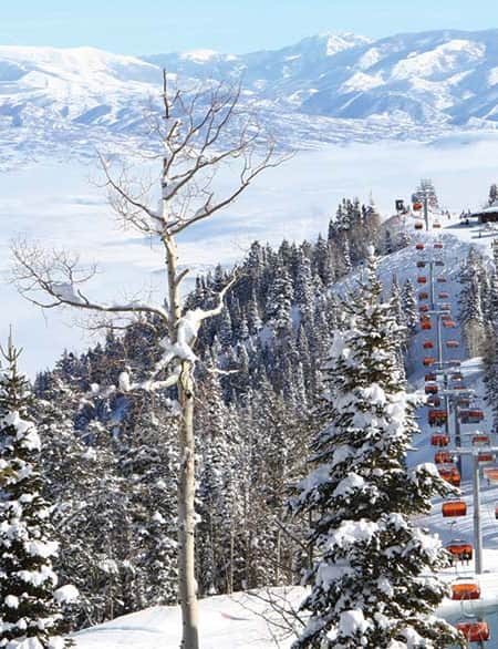 Skiers and snowboarders on ski lifts at Canyons Ski Resort in Park City, surrounded by snow-covered mountains.