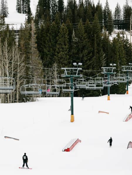 Skiers and snowboarders in the terrain park at Brighton Ski Resort, with a ski lift above them.