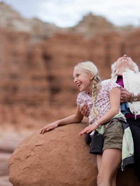A woman and young girl leaning against a red rock, laughing.