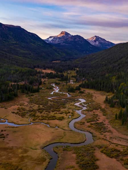 Two mountains with lush green trees framing a spacious valley with a river flowing through it.