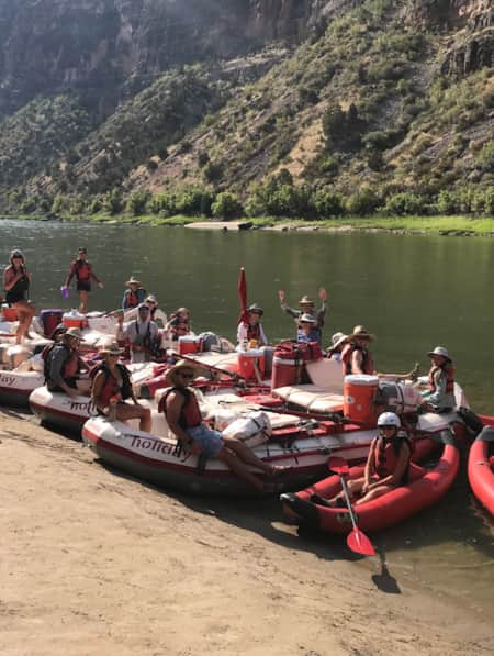 A group of rafters sitting on their rafts by the riverbank, laughing and enjoying themselves.