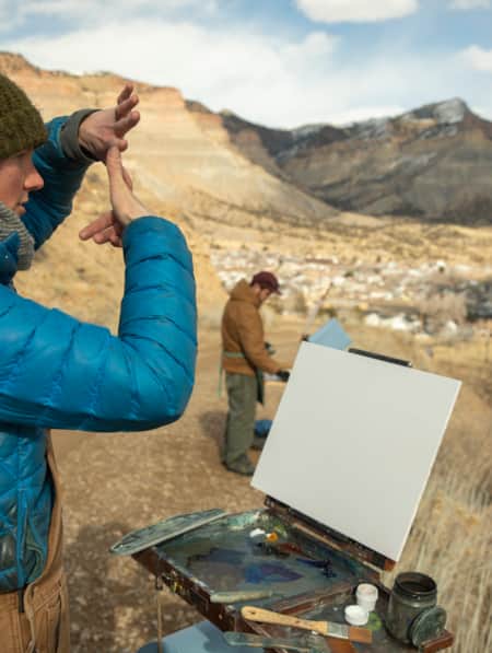 An artist with a canvas in front of them, observing the scenery and preparing to paint.