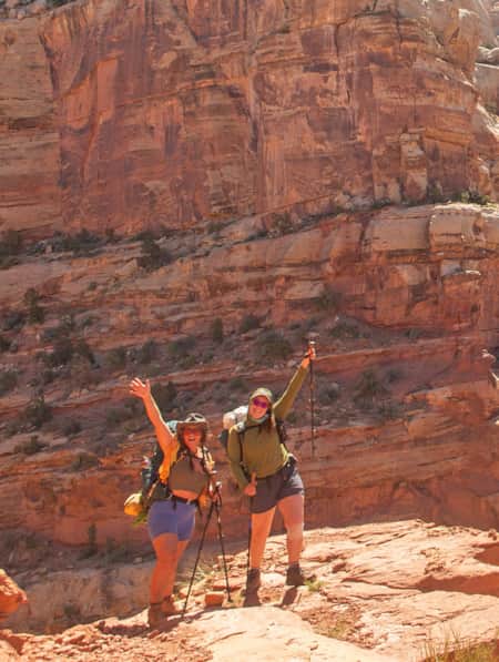Two female hikers smile and pose on a trail in Capitol Reef National Park.