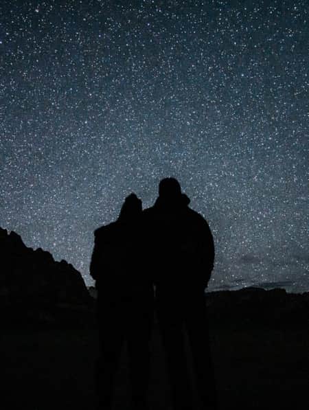 Two people stand in shadow beneath a bright starry sky in Zion National Park.