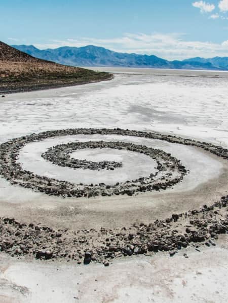 A spiral jetty extending into a salty lake during low tide, with a small brown hill visible in the distance.