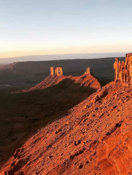 An expansive view of the desert with a large red rock monument glowing orange, illuminated by the sun.