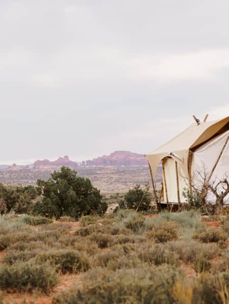 Canvas tent overlooking a desert landscape with red rock formations and green shrubbery.