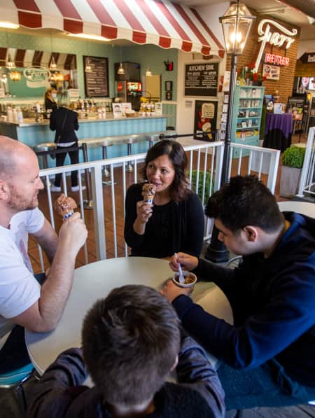 Two adults and two young children sitting at a table inside a creamery, each enjoying an ice cream cone.