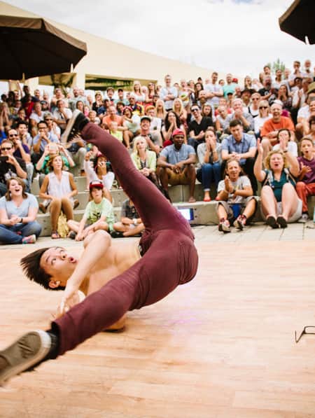 A man break dancing on a stage, surrounded by a cheering crowd.