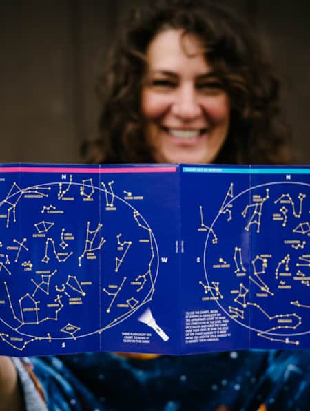 A woman holds a pamphlet with astrological signs on it.