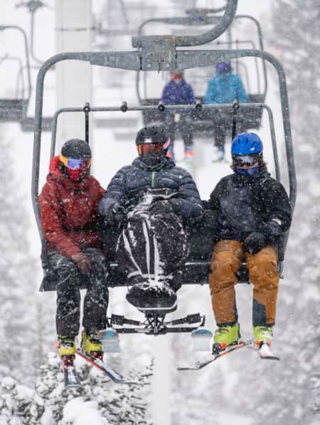 Three skiers sitting on a ski lift during a snowstorm, surrounded by heavy snowfall.