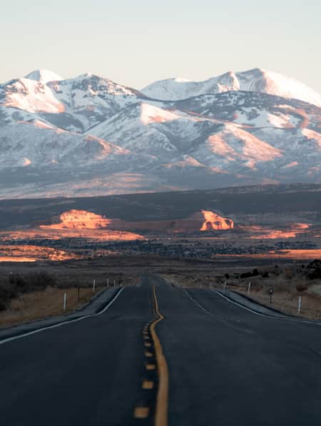 A long, straight paved road leading towards a snow-covered mountain range.